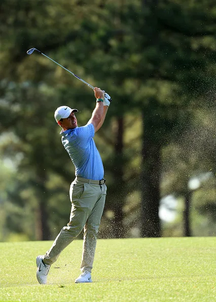 Rory McIlroy plays an approach shot with sand and grass spraying into the air