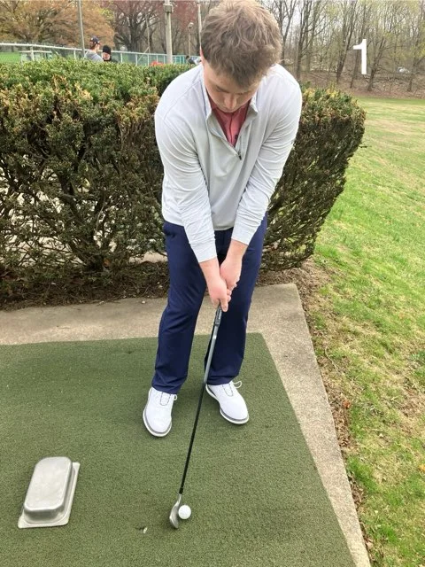 Golfer setting the ball near the trail foot with an overturned tray behind it